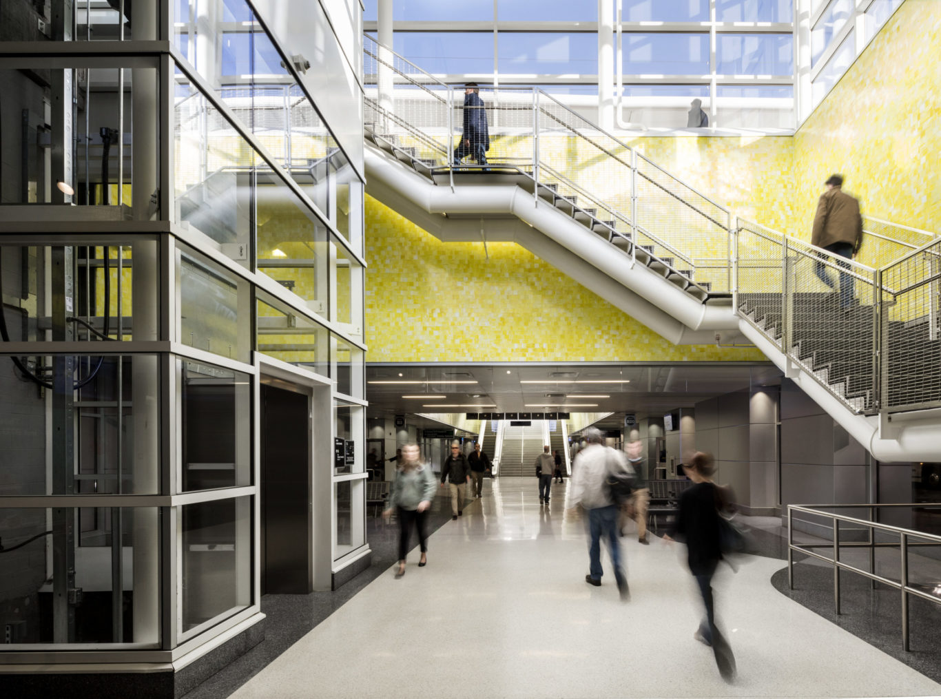 Slide 2 of 7, Underground, a 22-gate bus concourse services 16 regional, express, and local bus routes. The terminal, measuring 980 feet in length, serves a dual purpose as a pedestrian concourse that connects the constellation of transportation programs distributed across the site. Vivid colors and natural lighting help passengers orient themselves while handsome terrazzo floors and sparkling yellow glass tilework elevate the ambience of terminal beyond the often-unimaginative bus depot experience. A series of skylights and glass pavilions flood the hall with daylight, infusing the station with a sense of motion and spaciousness.  One of the largest projects of its kind in the United States, the redevelopment of the former rail yards at Denver Union Station is a case study of the power of transit-oriented urban design. This substantial public investment has catalyzed an unprecedented wave of private-sector activity. Sensitive to its historic location, but fundamentally forward looking in its technical sophistication and city-building spirit, Denver Union Station sets the standard for 21st-century intermodal hubs.