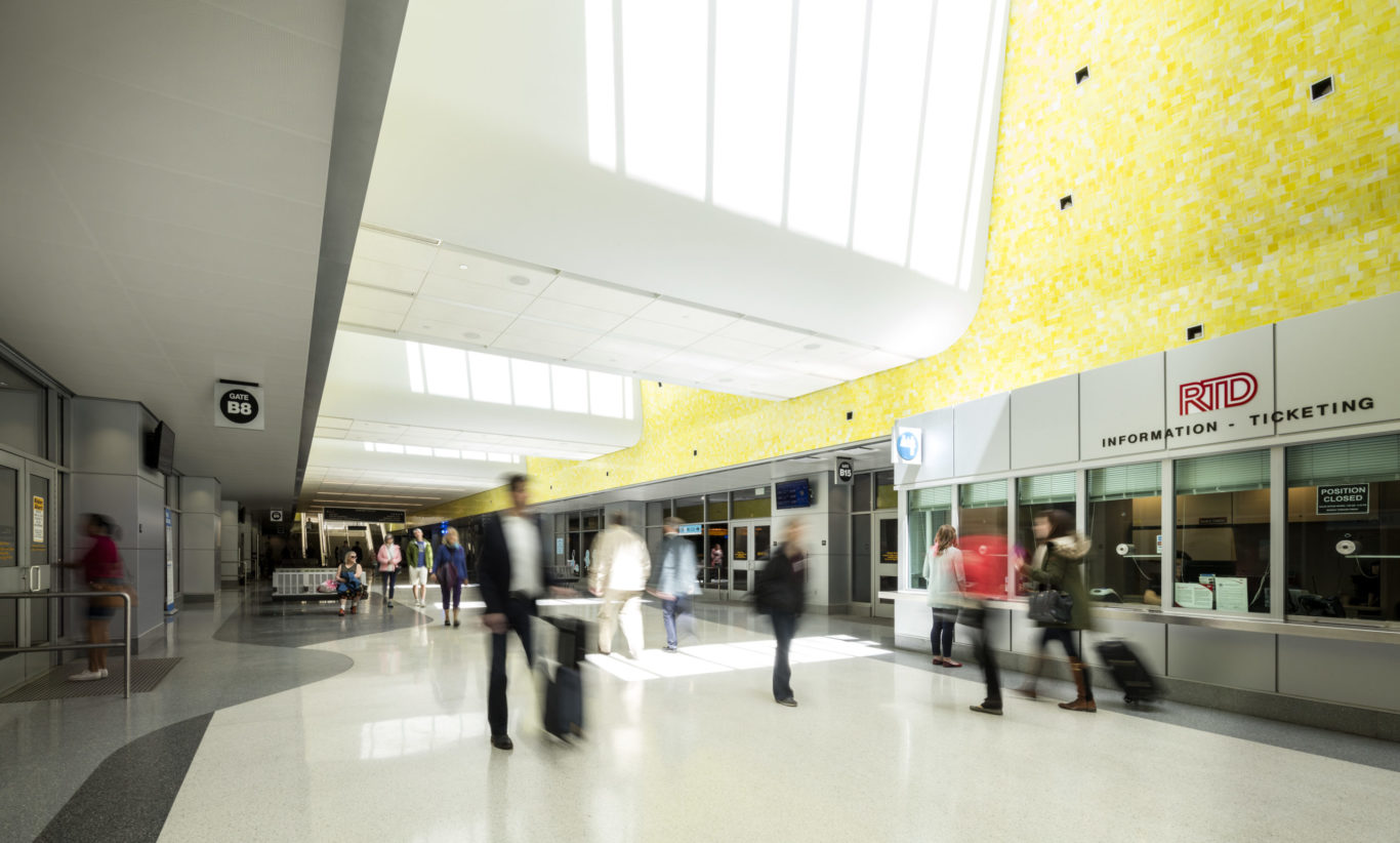 Slide 3 of 7, Underground, a 22-gate bus concourse services 16 regional, express, and local bus routes. The terminal, measuring 980 feet in length, serves a dual purpose as a pedestrian concourse that connects the constellation of transportation programs distributed across the site. Vivid colors and natural lighting help passengers orient themselves while handsome terrazzo floors and sparkling yellow glass tilework elevate the ambience of terminal beyond the often-unimaginative bus depot experience. A series of skylights and glass pavilions flood the hall with daylight, infusing the station with a sense of motion and spaciousness.  One of the largest projects of its kind in the United States, the redevelopment of the former rail yards at Denver Union Station is a case study of the power of transit-oriented urban design. This substantial public investment has catalyzed an unprecedented wave of private-sector activity. Sensitive to its historic location, but fundamentally forward looking in its technical sophistication and city-building spirit, Denver Union Station sets the standard for 21st-century intermodal hubs.